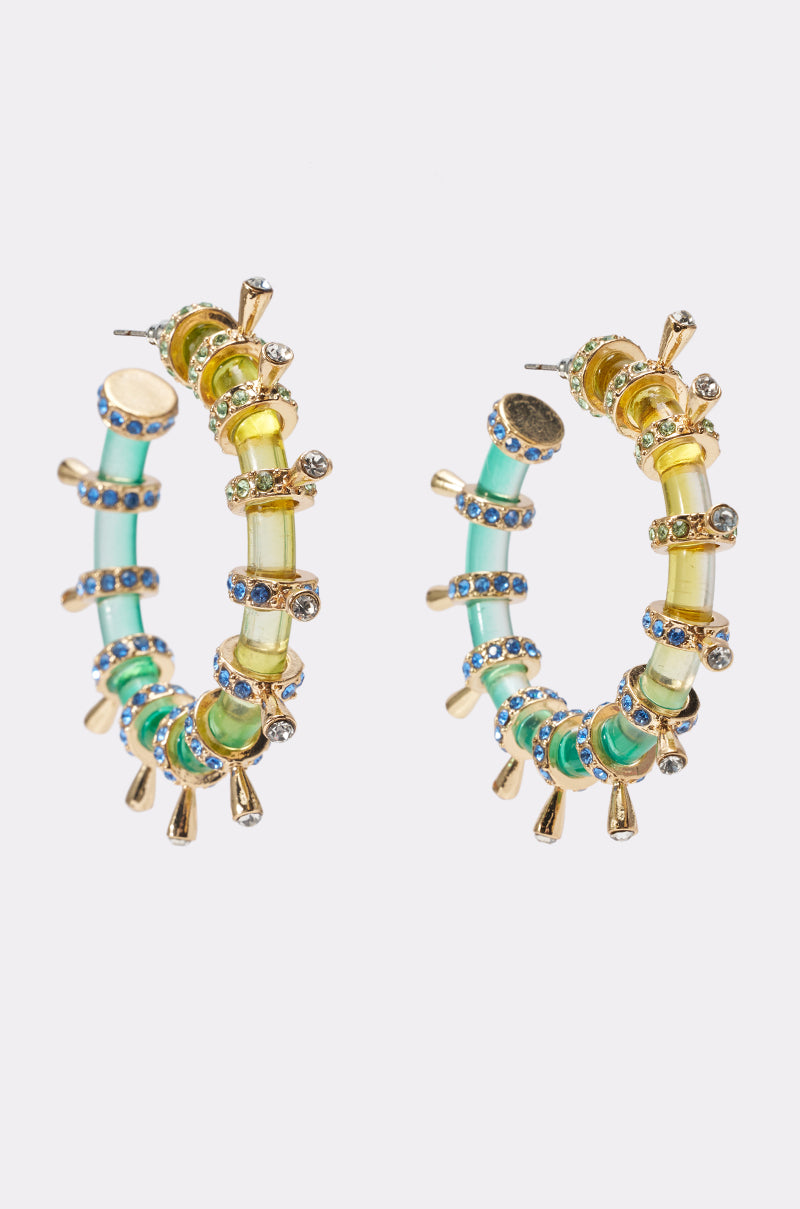 The FOR THE VIBES HOOP EARRING features ombre hoops with yellow and teal beads, blue gemstones, plus gold and silver accents—a vibrant, playful festival accessory shown against a white background.