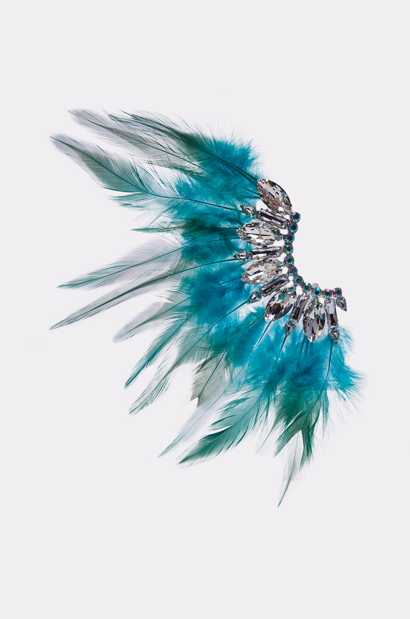 The FLY AWAY EARRING is a decorative accessory with vibrant blue and green feathers in a wing-like shape, accented by a central band of sparkling rhinestones for added glamour.
