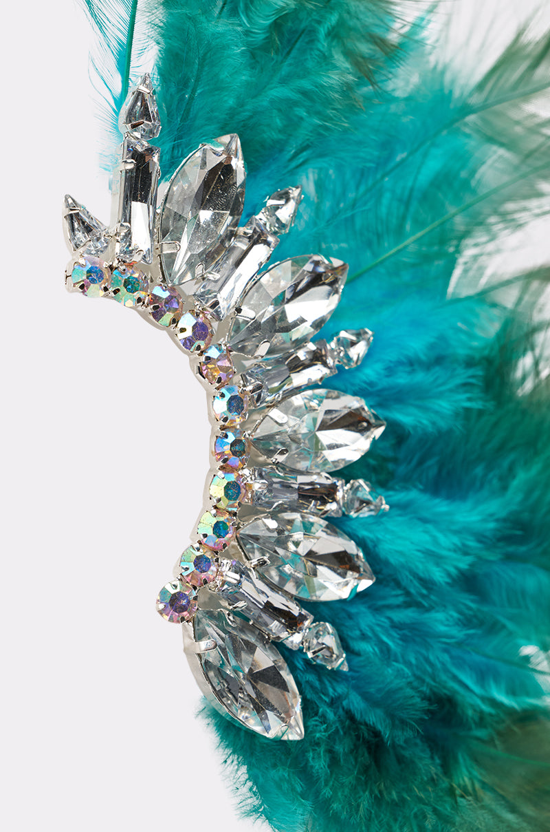 A close-up of the FLY AWAY EARRING, a statement accessory with clear and iridescent rhinestones in a curved design, accented by vibrant teal feathers—ideal for anyone seeking bold teal feather earrings. 3