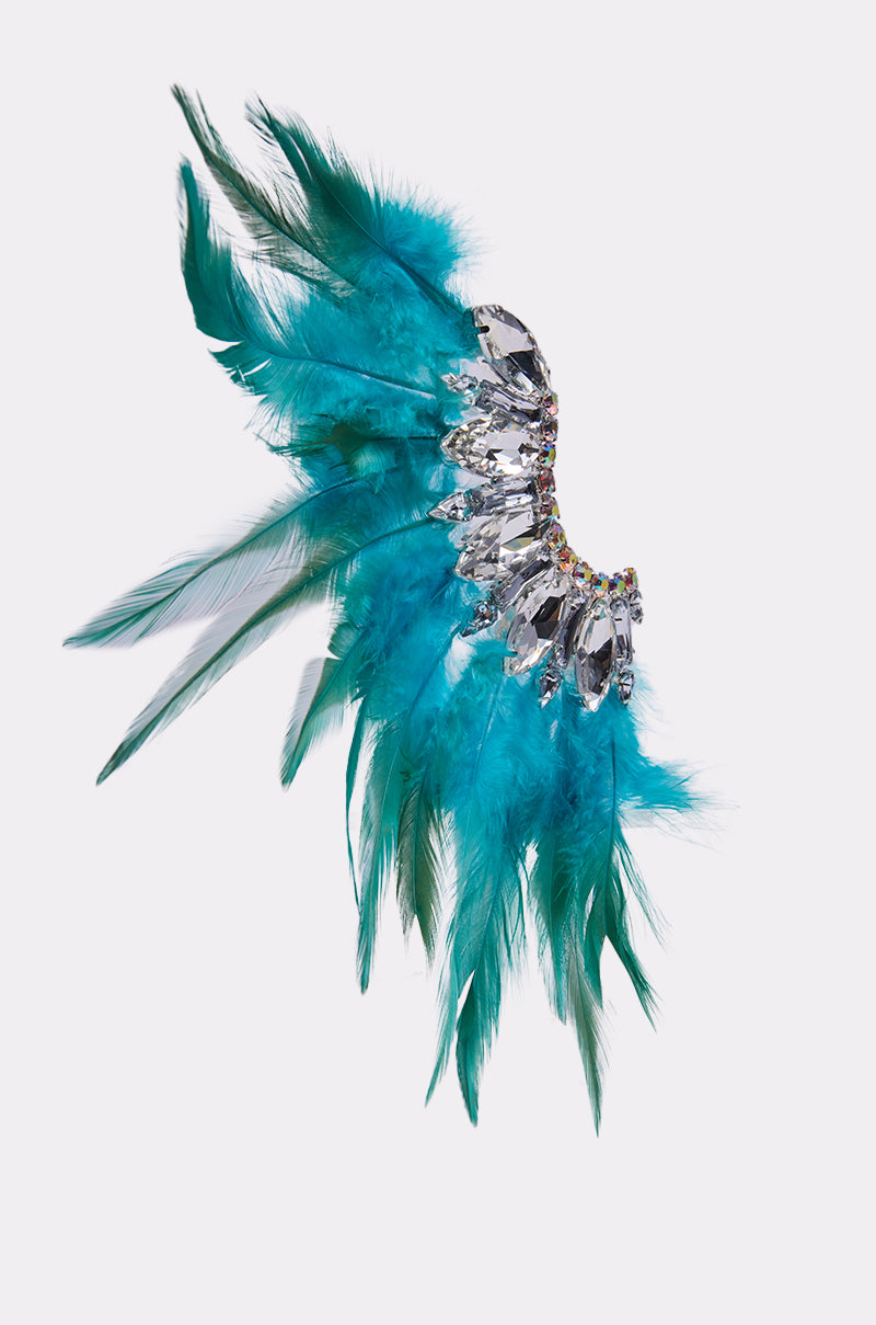 The FLY AWAY EARRING showcases vibrant turquoise and green feathers in a fan shape, accented with sparkling clear gemstones and rhinestones at the base for an extra touch of glamour.