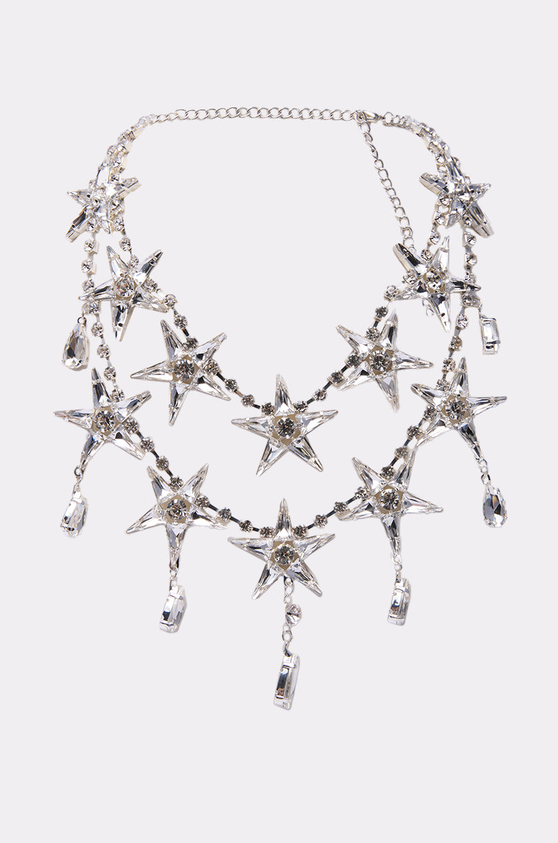 The STARGURL NECKLACE is a silver celestial accessory with three layered chains, each embellished with large rhinestone starburst pendants and teardrop crystal dangles.