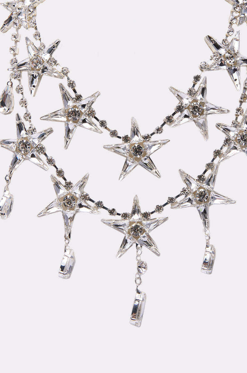 A close-up of the STARGURL NECKLACE, featuring silver star-shaped designs with clear gemstones, rhinestone starburst accents, and hanging rectangular crystal pendants, set against a plain white background. 2
