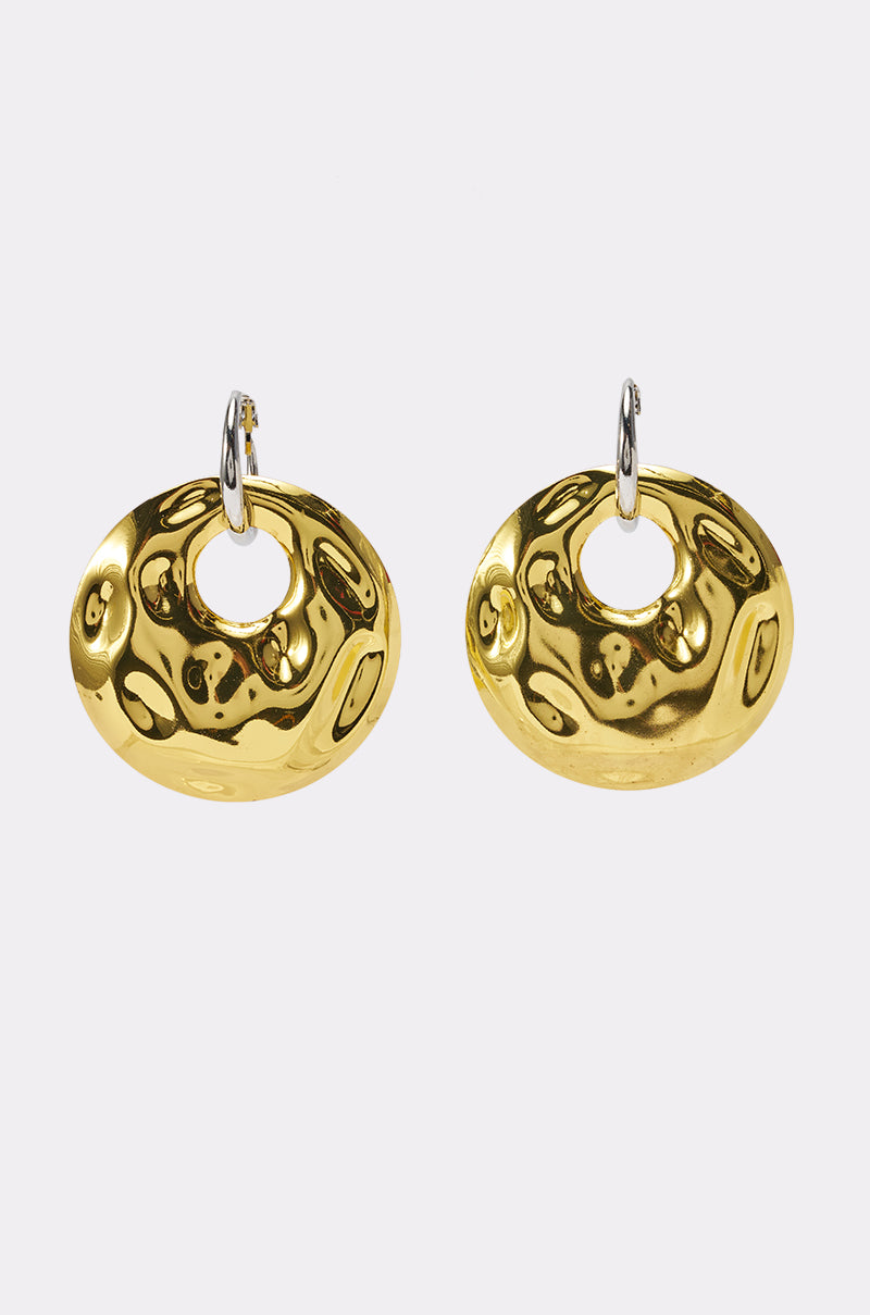 The OVERSIZED 2-TONE STATEMENT EARRING features shiny, hammered gold-tone oval pieces with small circular openings at the top, attached to silver hoops for a bold and striking two-tone design, showcased on a plain white background.