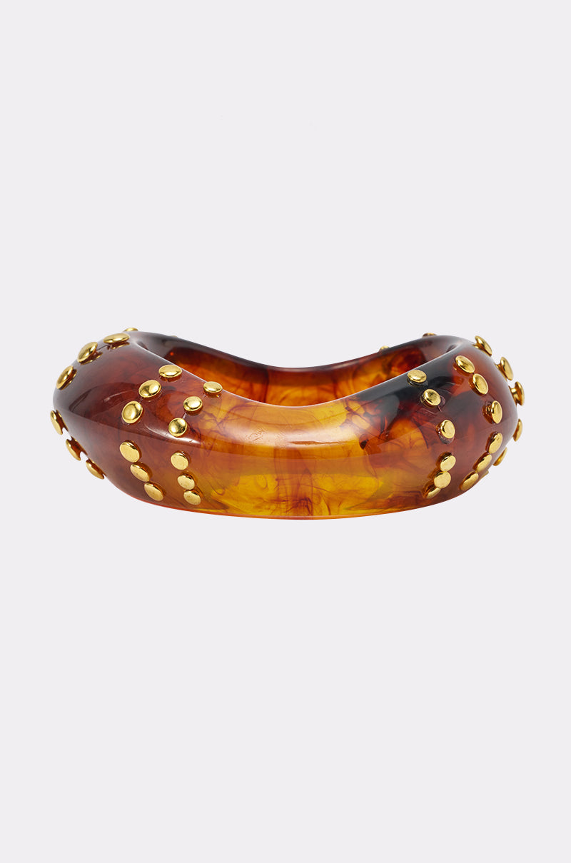 The COOL GIRL STUDDED BANGLE IN BROWN is a chunky, marbled amber and brown resin acrylic bracelet featuring gold stud accents, shown against a plain white background.