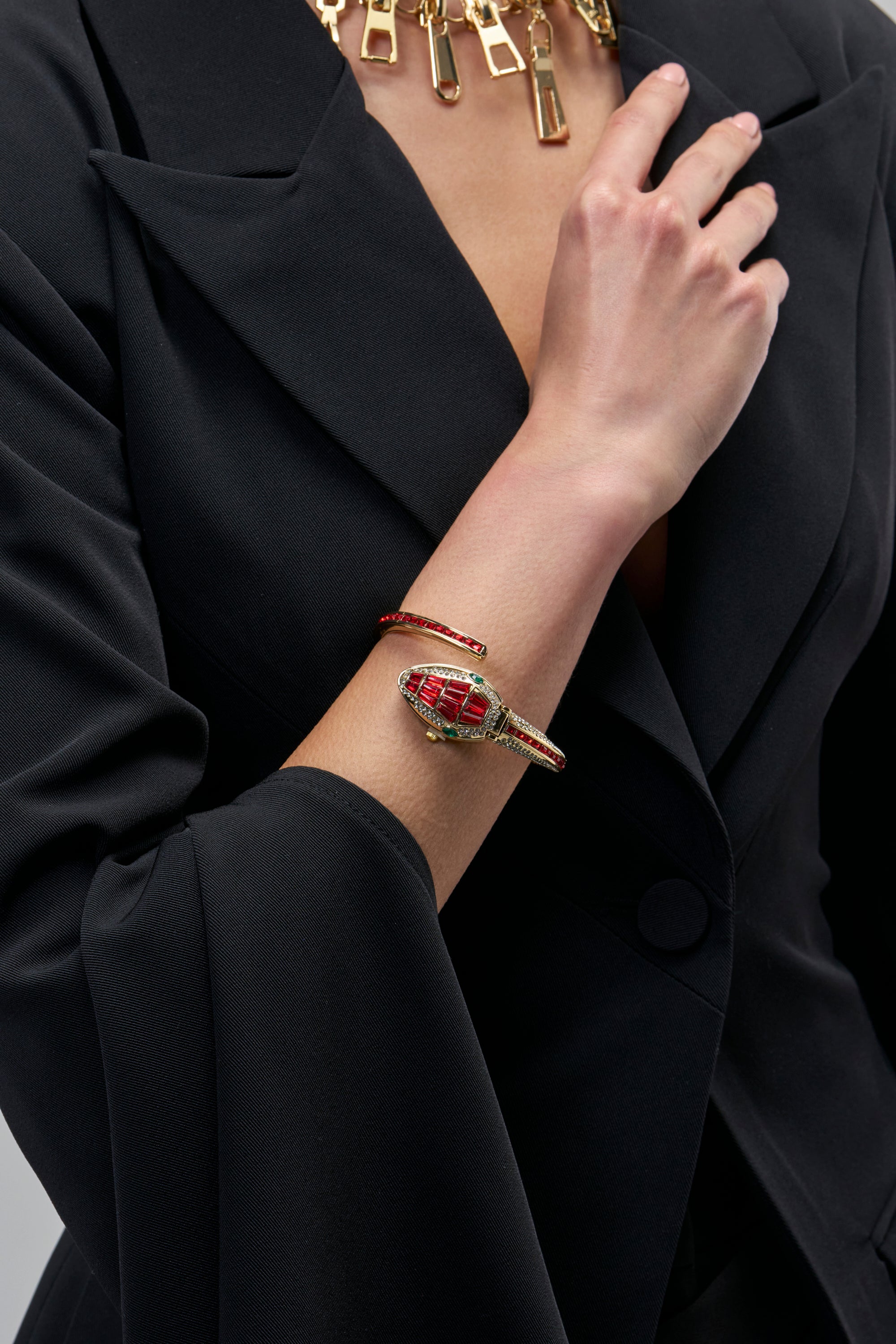 VENOM KISS WATCH IN RED gold serpent cuff watch with red crystal scales wrapped around a person’s wrist.