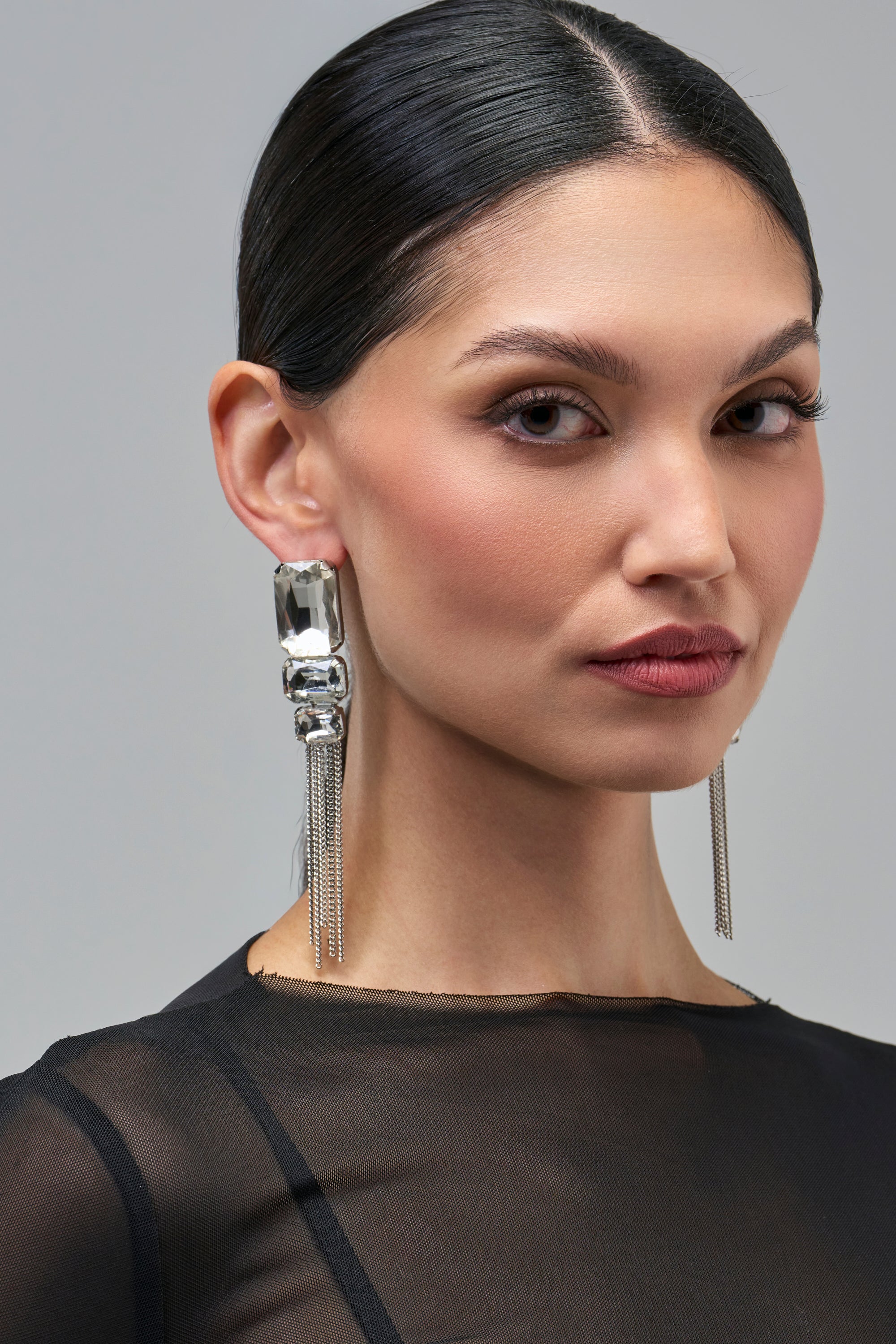 A woman wearing ALL EYES ON ME EARRINGS, which feature silver stacked rectangular crystals and dangling chains.
