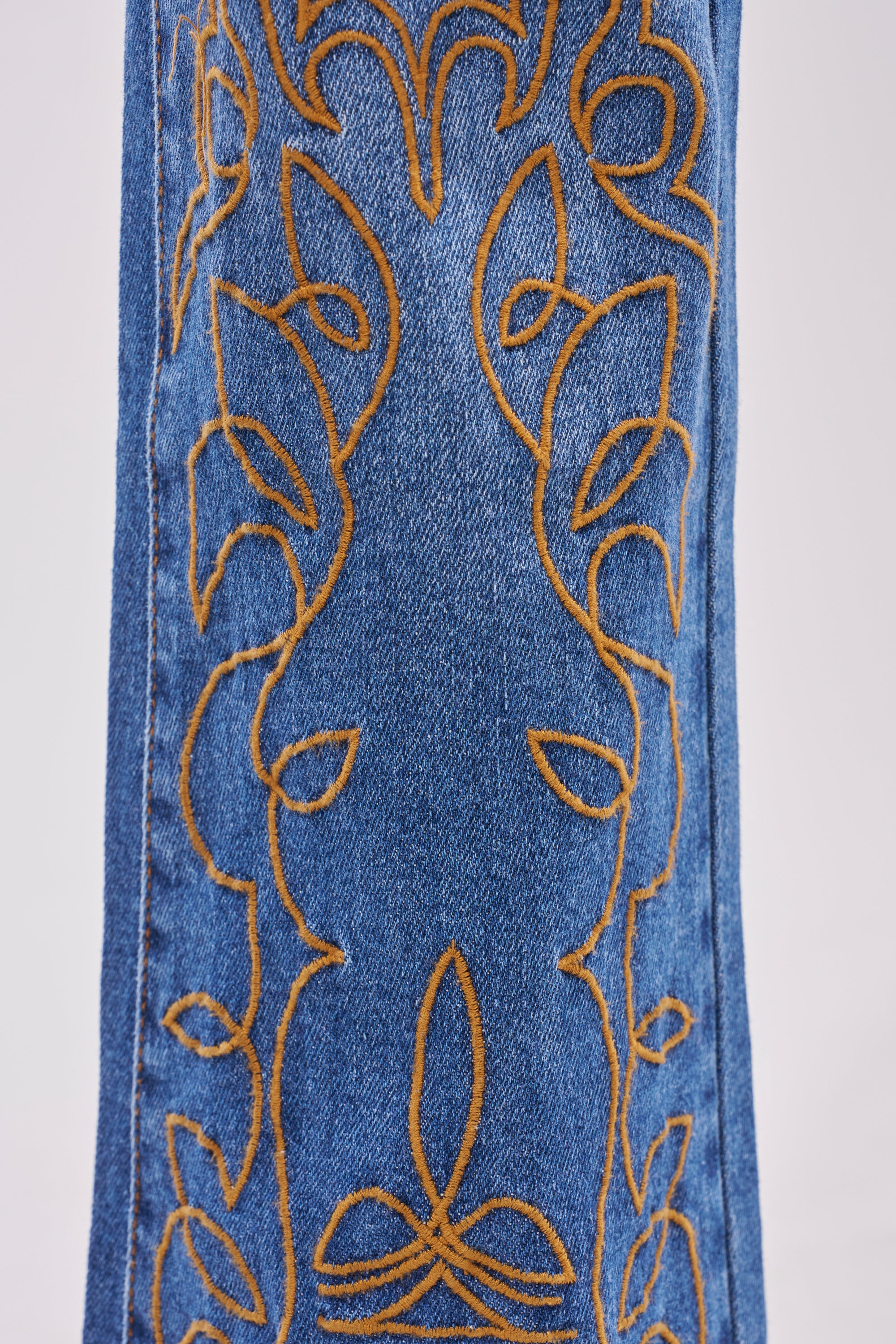 Close-up of medium-wash RODEO BABE SKINNY FLARED DENIM, detailed with intricate orange embroidery in flowing, leaf-like vertical patterns—ideal for flared skinny or embroidered hem jeans styles. 5