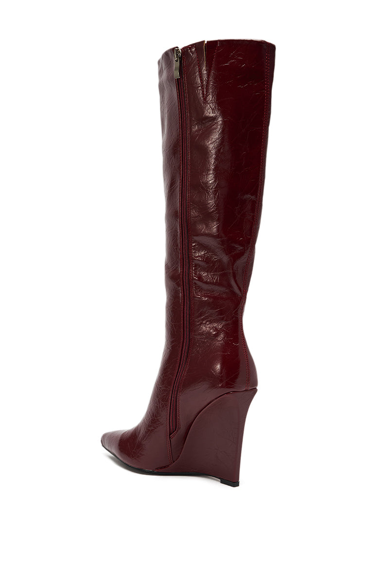 The AZALEA WANG AMAADIS BURGUNDY WEDGE KNEE HIGH BOOT features rich burgundy faux leather, a side zipper, and a shiny wedge heel, shown in a side view against a white background.