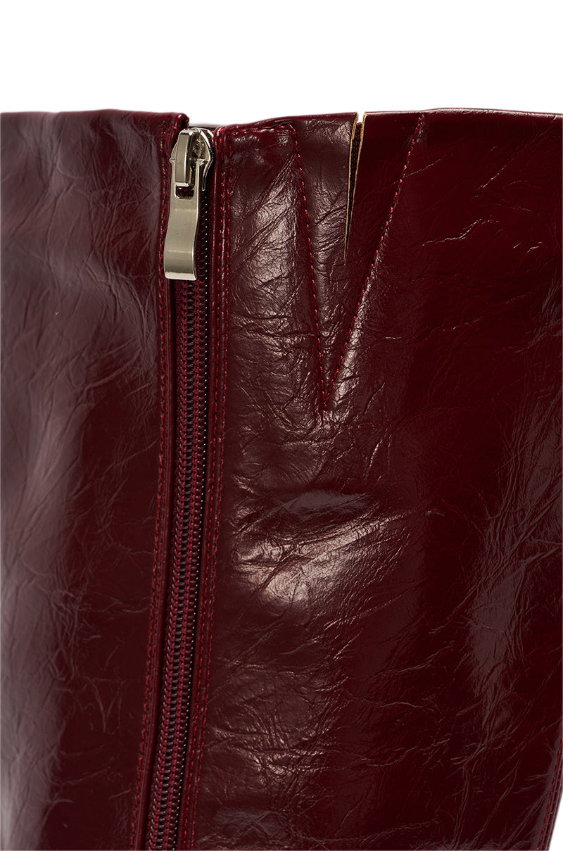 Close-up of the AZALEA WANG AMAADIS Burgundy Wedge Knee High Boot, featuring shiny dark red faux leather, a visible side zipper, a V-shaped notch near the top edge, and a stylish wedge heel.