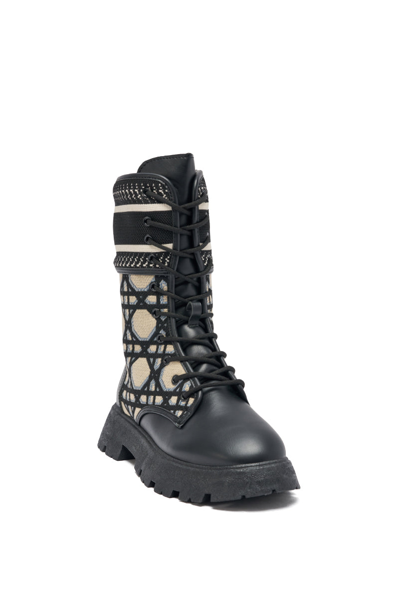The AMADA CANVAS PRINT COMBAT BOOT features black canvas, thick laces, a chunky sole, and a tan panel with geometric circular print and black overlays. These streetwear boots stand out against a white background.