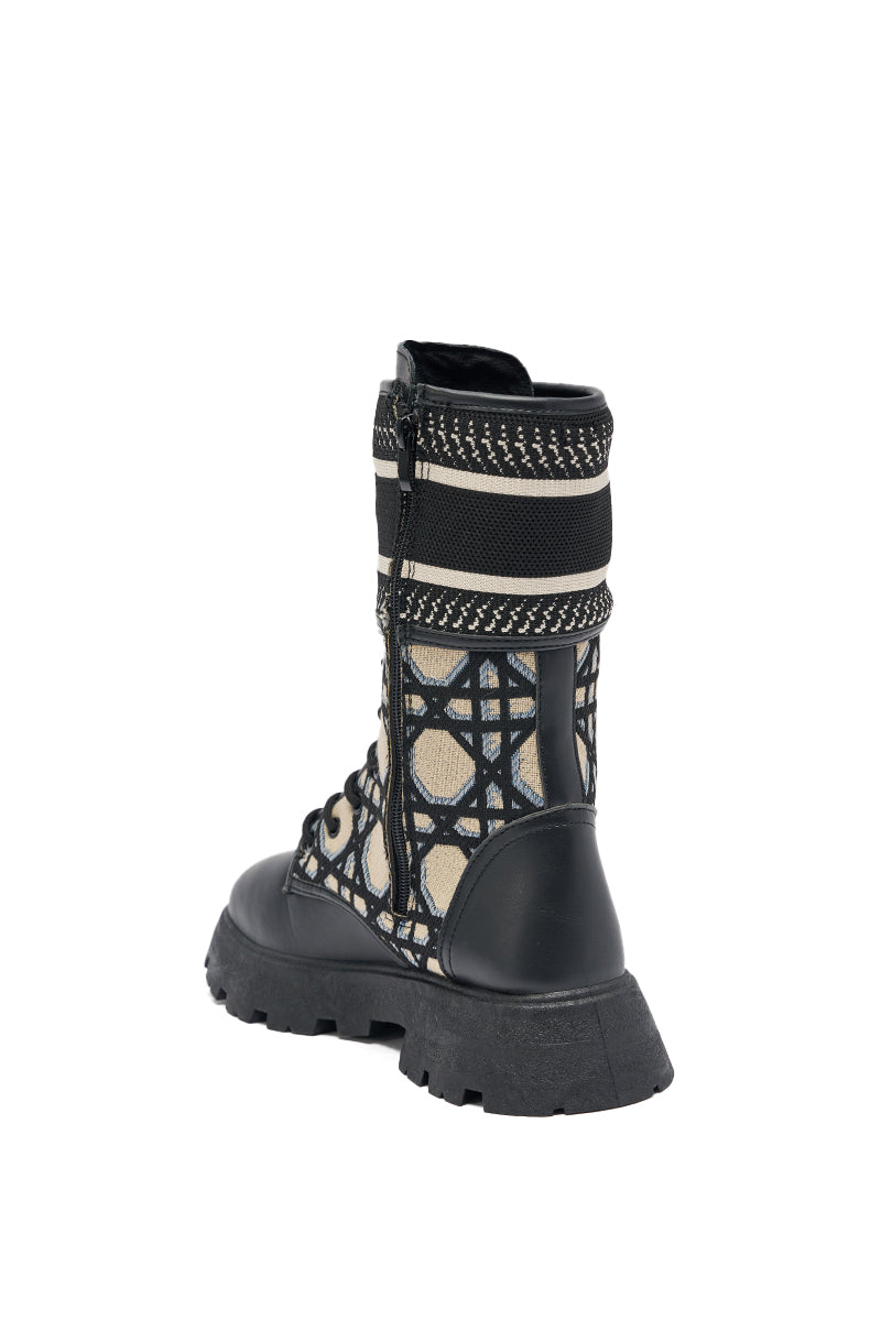 The AMADA CANVAS PRINT COMBAT BOOT features black lace-up streetwear style, a thick rugged sole, and beige patterned canvas panels, displayed from a rear-side angle on a white background.