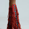Against a plain background, a person wears the AZALEA WANG AMADEO RED SANDAL—red knee-high fringe boots with turquoise gemstone embellishments. These open-toed gladiator-style sandals offer a unique and stylish edge.