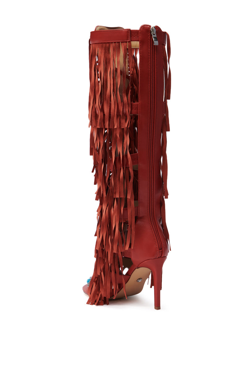 The AZALEA WANG AMADEO RED SANDAL is a red, open-toe, knee-high gladiator sandal with fringed vegan leather straps, a back zipper closure, stiletto heel, and cascading fringe detailing on the side.