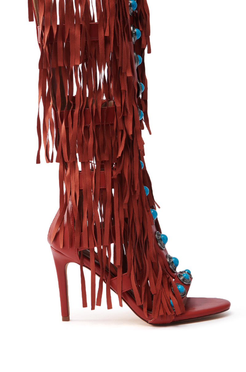 The AZALEA WANG AMADEO RED SANDAL is a red high-heeled gladiator sandal made from vegan leather, featuring long cascading fringes and blue spherical ornaments on the front strap, completed with an open toe and stiletto heel.