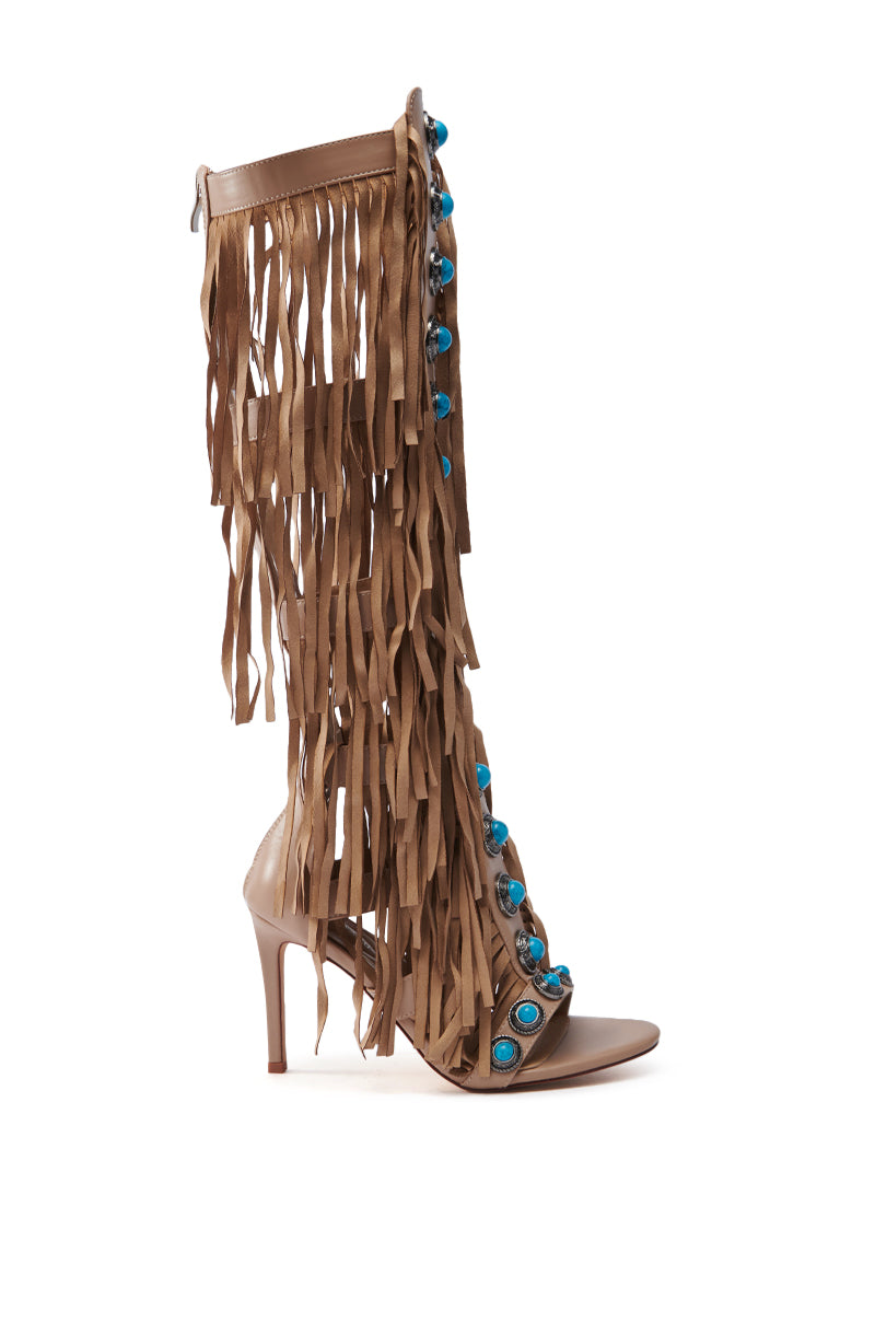 The AZALEA WANG AMADEO TAN SANDAL is a faux leather gladiator sandal with a stiletto heel, long fringes, and turquoise embellishments along the front. It features an open toe design and has a back zip closure for easy wear.
