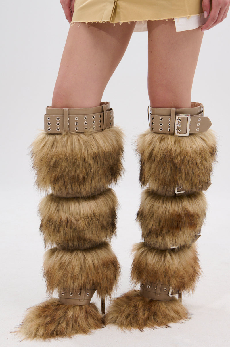A person wearing a tan mini skirt and AZALEA WANG AMALBERT BROWN MULTI FUR AND BUCKLES BOOT stands against a plain white background.
