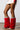 A person stands on a smooth floor, showcasing a short cream skirt paired with the AZALEA WANG AMOURA RED FUR AND SNAKE BOOT, featuring red furry leg warmers with snake-patterned details and knee-high design.