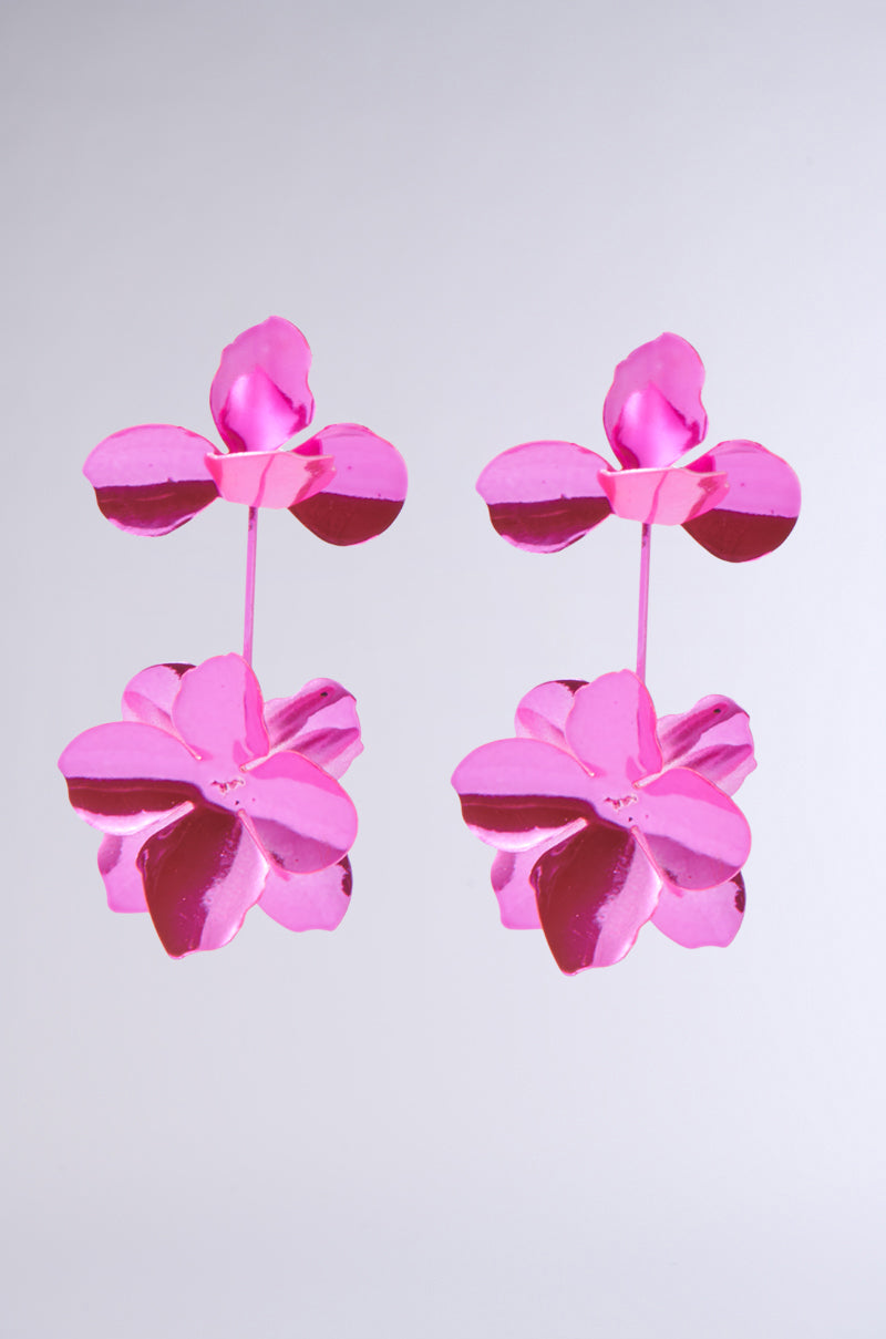 Two ASH FLOWER EARRINGS in hot pink metal, featuring layered petals, shimmer against a plain gray background. The reflective metal design gives them a bright and vibrant appearance. 2