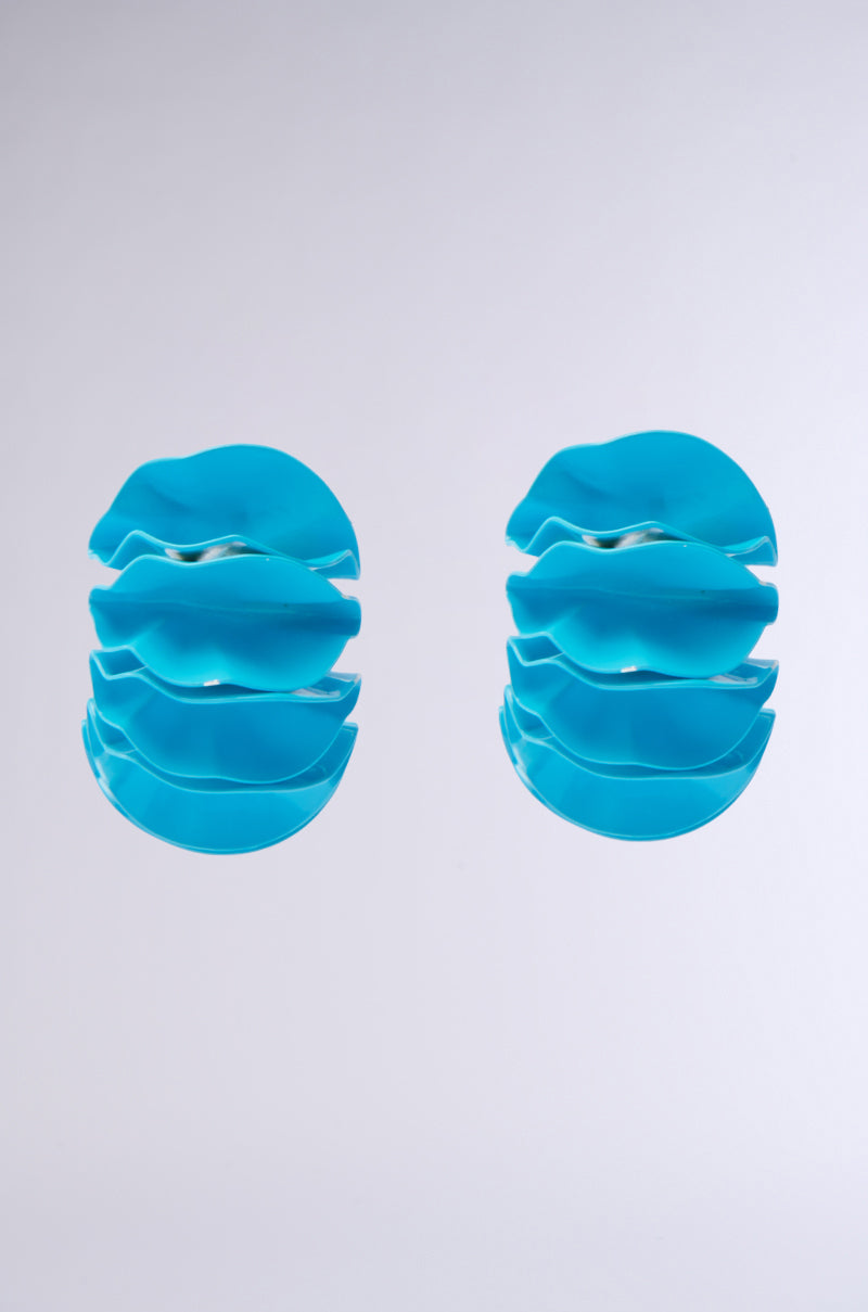 The FANNED OUT EARRING features a modern aesthetic with abstract blue sculptural spirals, layered wavy shapes on a white background, and a smooth texture.