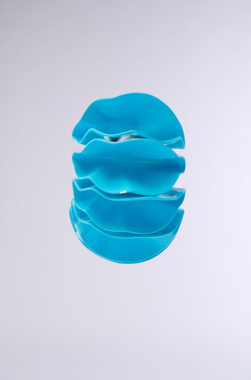 A sky blue abstract sculpture features stacked wavy metal shapes against a light gray background. The fluid, ripple-like pattern and glossy material are reminiscent of the FANNED OUT EARRING.