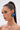 A woman with long, dark hair in a high ponytail wears dramatic eye makeup and striking DENIM BLUE EARRING studs. She poses against a plain light background, gazing to the side with a calm expression.