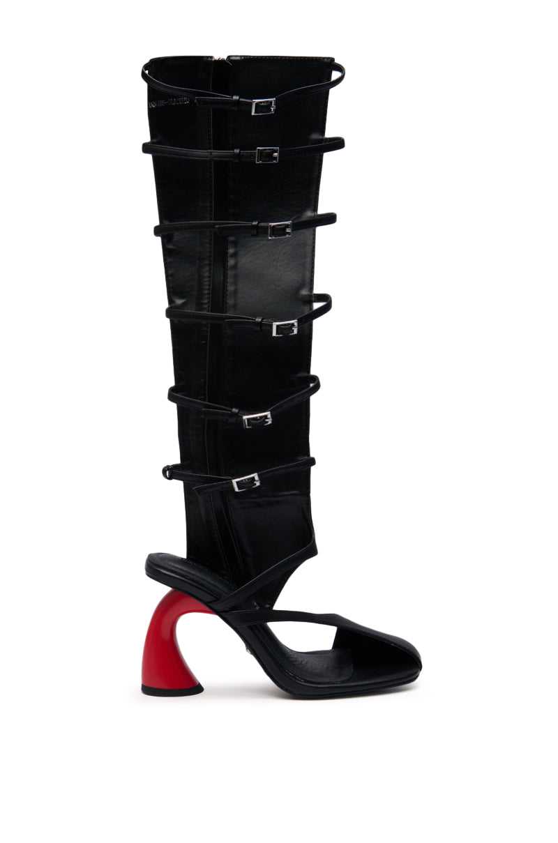 The AZALEA WANG ANDRIUS Black with Red Heel Gladiator Sandal is a tall faux leather boot featuring multiple thin buckle straps, an open toe, and a distinctive curved red and black high heel.