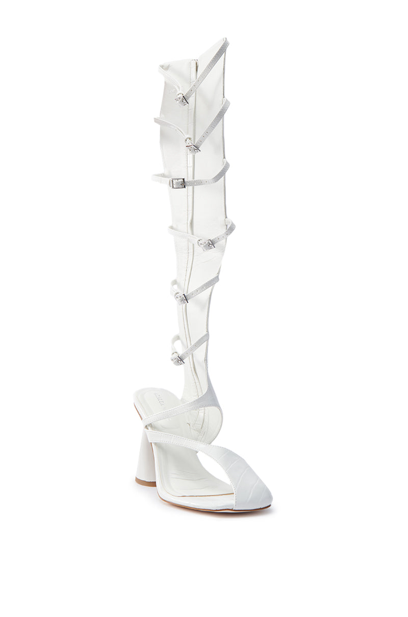 The AZALEA WANG ANDRIUS WHITE CROC CHUNKY GLADIATOR SANDAL features a white high-heeled, croc-embossed faux leather finish with strappy knee-high details, multiple buckles and embellishments. Its open-toe design and sturdy block heel are perfect for fans of bold chunky gladiator styles.