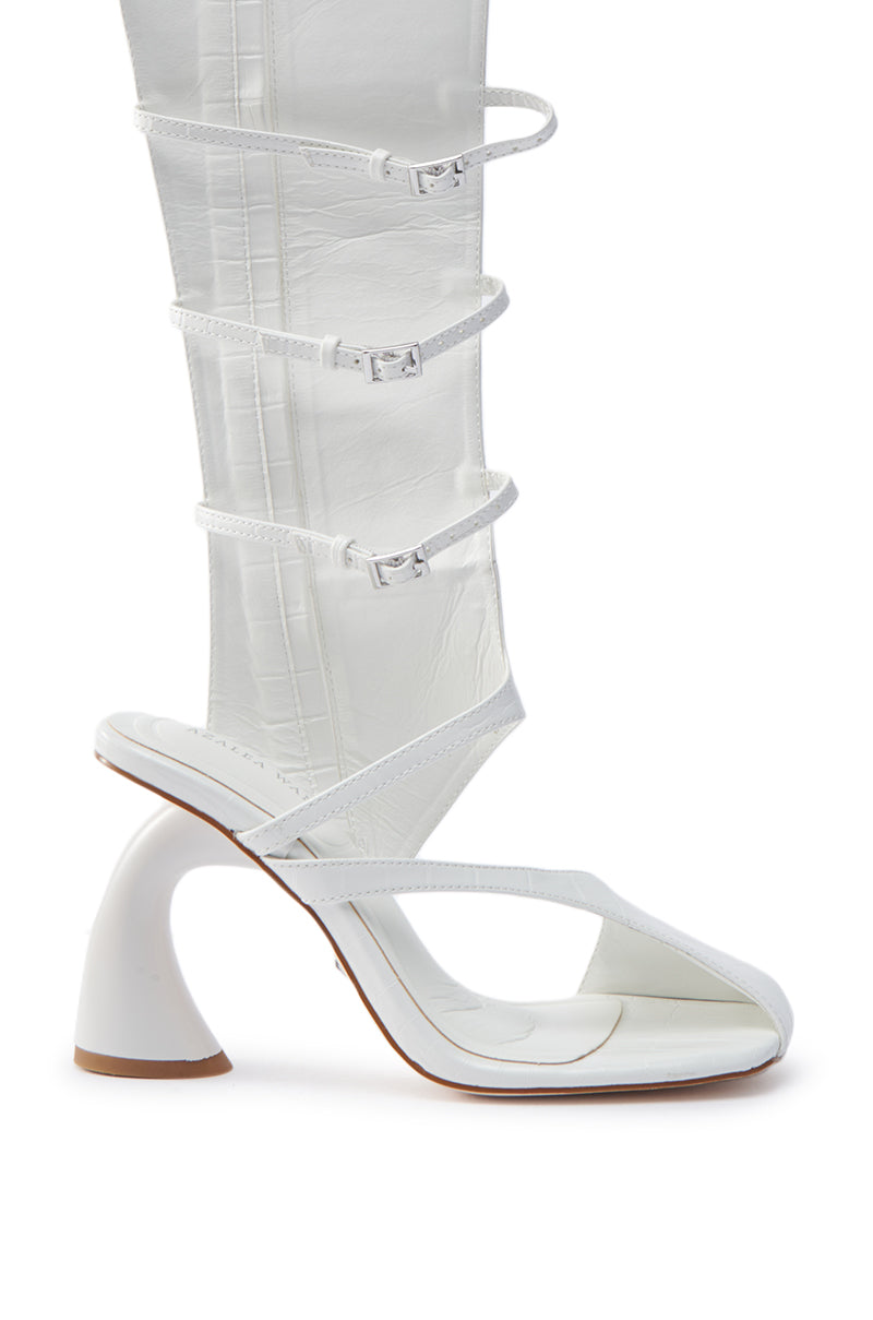 The AZALEA WANG ANDRIUS WHITE CROC CHUNKY GLADIATOR SANDAL is a high-heeled, knee-high gladiator with a distinctive curved heel. Made from croc-embossed faux leather, it features white straps and buckle fastenings, merging the sleek style of sandals and boots.