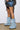 A person wearing frayed denim shorts stands on a tan floor against a white background, showcasing the AZALEA WANG ANGELA Fold Over Platform Boot in Denim. These oversized light blue boots feature chunky flatform soles, are slouchy, and cover most of the lower legs.