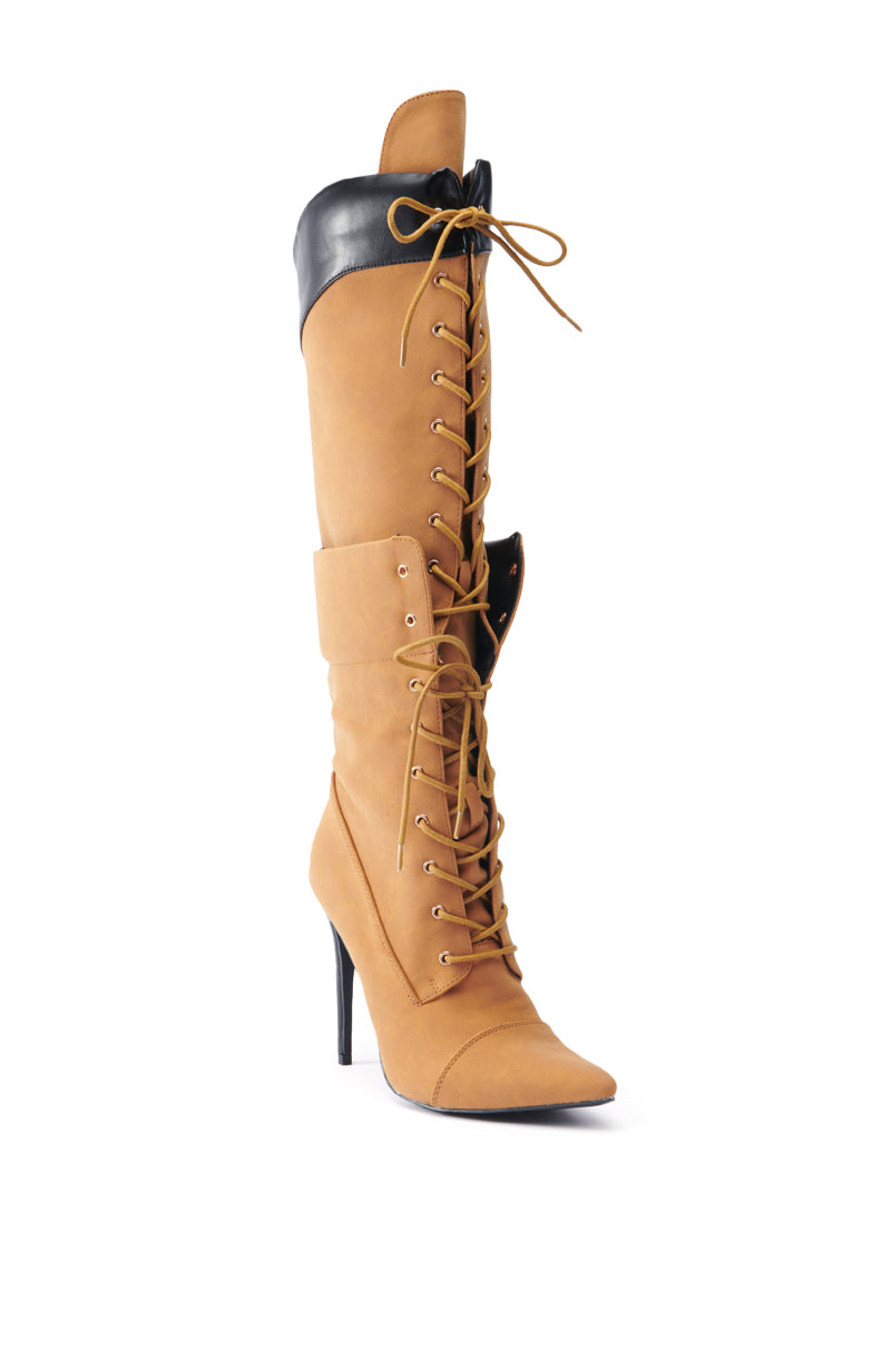 The ANNAMARIE BROWN STILETTO BOOT is a knee-high stiletto fashioned from faux leather, complete with striking black trim and lace-up detailing. It boasts a pointed toe and high heel, all beautifully displayed against a white backdrop.