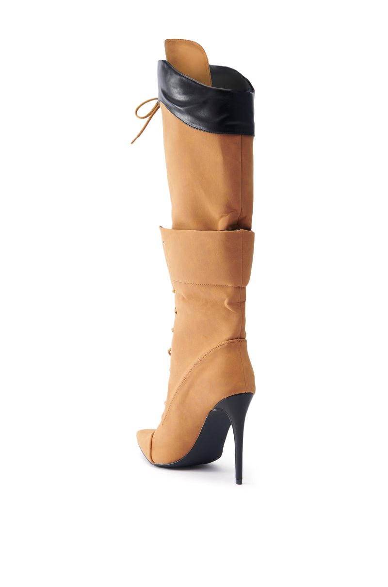 The ANNAMARIE BROWN STILETTO BOOT features a stylish tan color with knee-high length, complemented by a high heel and a black faux leather cuff at the top. This elegant design includes a lace-up pattern and pointed toe, highlighted in a three-quarter side view.