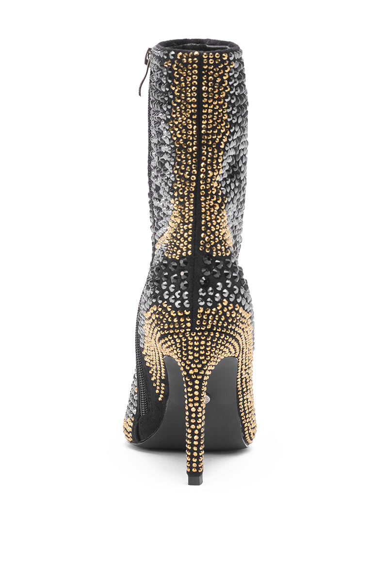 The AZALEA WANG ANSLEY BLACK MULTI RHINESTONE COCKTAIL BOOTIE is a black suede ankle boot with a stiletto heel, adorned with gold and silver studs, shown from the back against a white background.