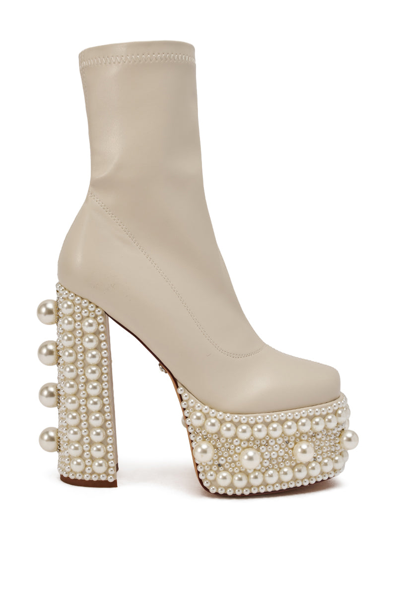 The AZALEA WANG ANTARIS BEIGE PEARL DETAIL PLATFORM BOOTIE is a beige faux leather, high-heeled bootie with a chunky heel and platform, finished with white pearl accents in multiple sizes. 5