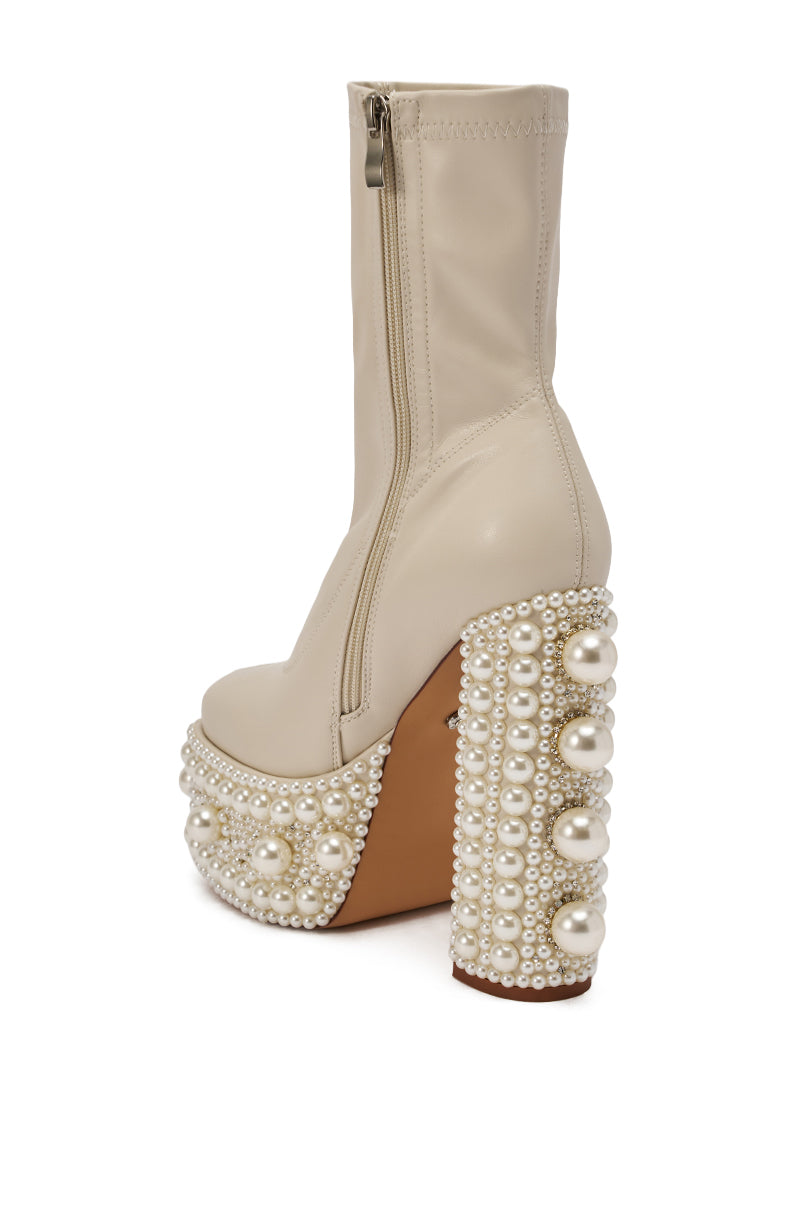 The AZALEA WANG ANTARIS Beige Pearl Detail Platform Bootie is a high-heeled faux leather ankle boot with a side zipper, chunky heel, and platform adorned with multiple rows of large and small white faux pearls. 7