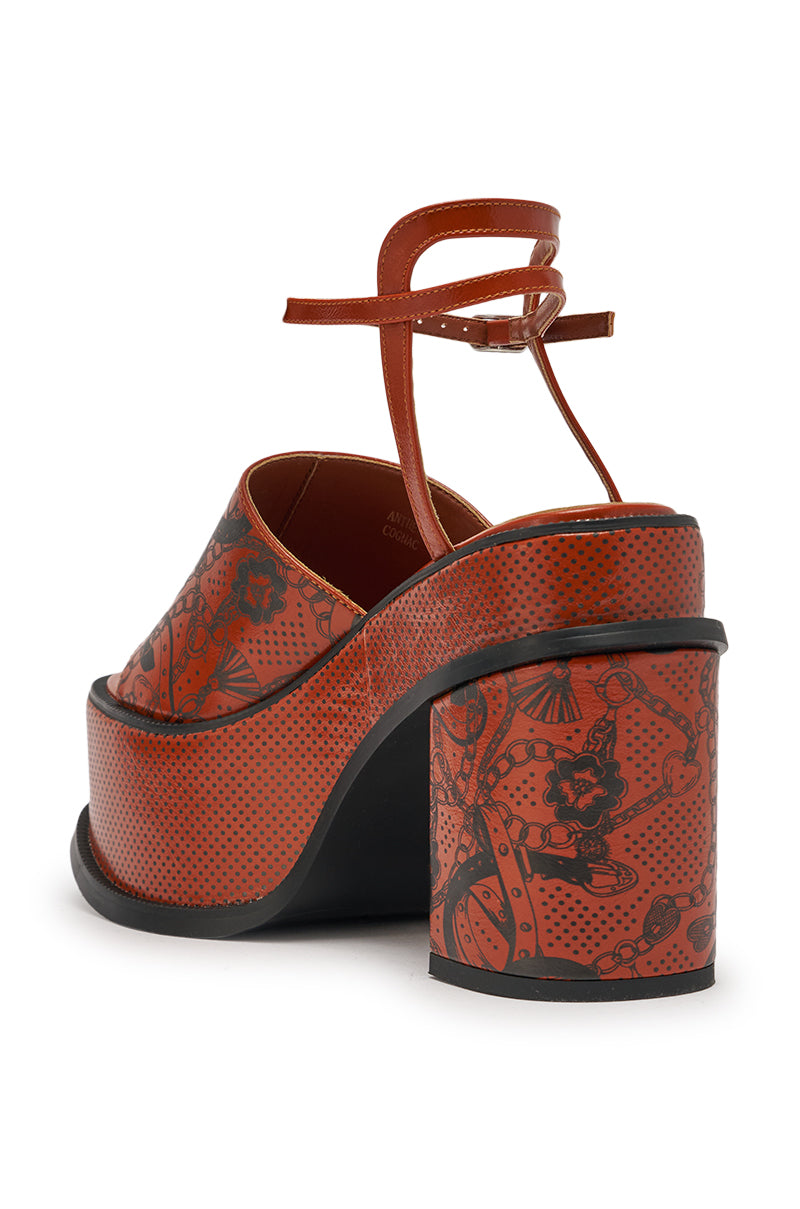 Rear view of the AZALEA WANG ANTHELMINE COGNAC platform sandal, featuring brown faux leather, a chunky block heel, ankle strap, and a red base with black tattoo-inspired floral and dotted detailing. 5