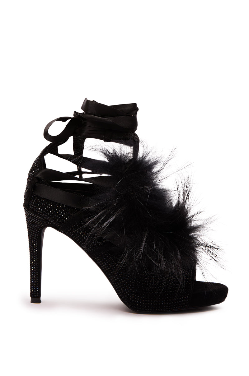 The AZALEA WANG ANTIRI Black Sparkle and Fur Sandal features high heels, black feathers, satin ankle ties, and sparkling accents on the stiletto heel and sole, showcased against a white background.