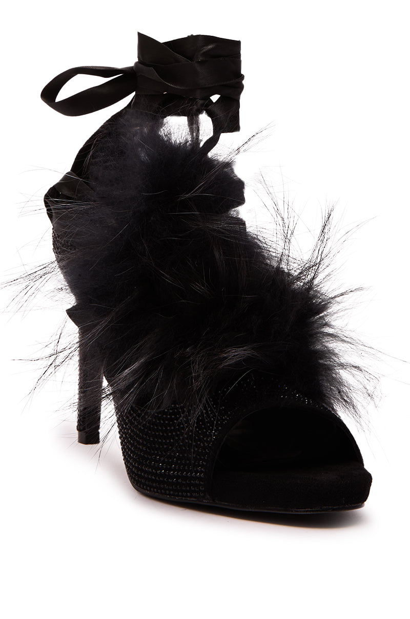 The AZALEA WANG ANTIRI BLACK SPARKLE AND FUR SANDAL is a stiletto heel with an open toe, black feathers, rhinestones, and a ribbon ankle tie—perfect for standout style.