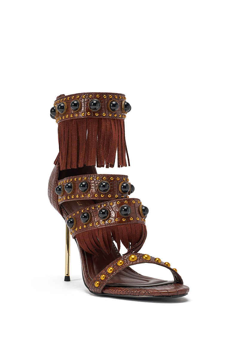The AZALEA WANG ANTOINE Brown Fringe and Gold Embellished Stiletto Heel features brown leather straps, fringe, black and yellow gem accents, and a slim metallic gold heel, displayed against a white background. 5
