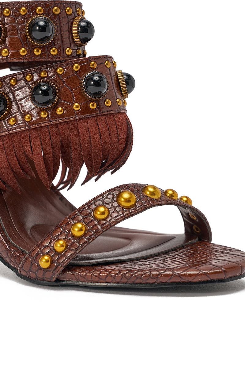Close-up of the AZALEA WANG ANTOINE BROWN FRINGE AND GOLD EMBELLISHED STILETTO HEEL, crafted in croc-embossed faux leather with gold studs, a reptile-like texture, and a fringed ankle strap. 7