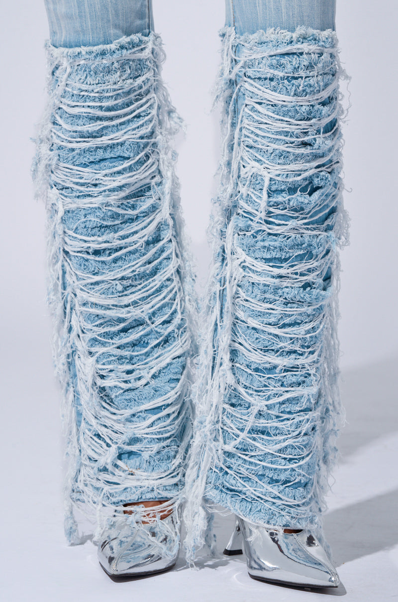 A close-up image features legs clad in the "STOP AND STARE DENIM PANT," showcasing light wash denim with heavy distressing and extensive shredded detailing. These high-rise jeans are paired with metallic, pointed-toe high heels against a plain light grey background.