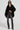 A woman confidently poses in the STACKS ON STACKS DENIM PANT, paired with a black draped top and dark sunglasses. She accessorizes her look with layered silver necklaces and black ankle boots, standing against a plain background and exuding effortless style.