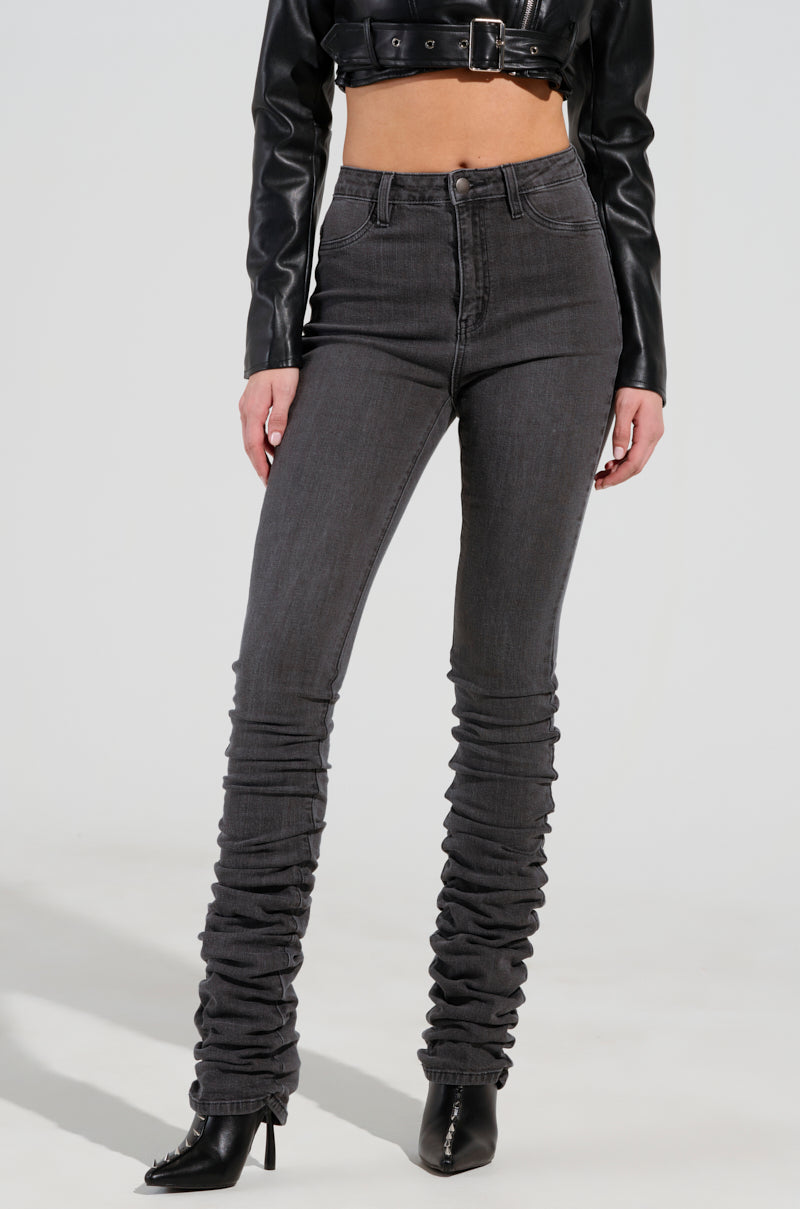 A person wearing STACKS ON STACKS high-rise skinny leg denim pants in gray and a black cropped leather jacket stands against a plain background, their feet clad in black high-heeled boots. 0
