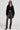 A person wearing dark sunglasses, a black oversized shirt, a cropped top, the STACKS ON STACKS DENIM PANT in high-rise gray skinny fit, and black pointed-toe boots. They have long dark hair and accessorize with layered necklaces and earrings against a plain white background.