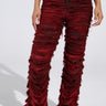 Someone in shredded ON FIRE DISTRESSED DENIM PANT, a red mid-rise design with frayed texture, pairs it with leopard print slip-ons against a plain backdrop. The high-waisted pants offer a stylish look, while the top is partially visible.