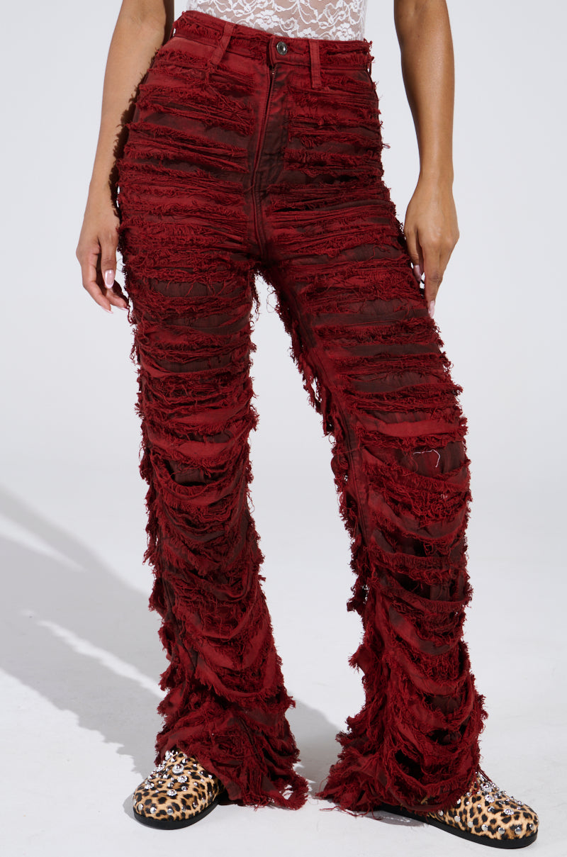 A person models the ON FIRE DISTRESSED DENIM PANT in red, showcasing horizontal rips that reveal a white underlayer, paired with a white lace top and leopard print shoes against a plain white background.