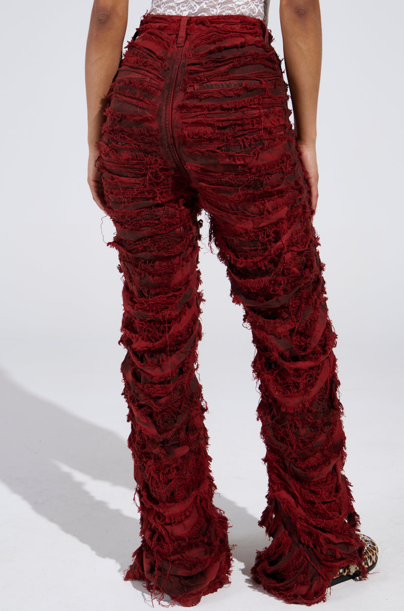 A person is wearing ON FIRE DISTRESSED DENIM PANT in deep red, featuring a high-waisted design and frayed detailing. Paired with a white top, they stand against a plain background.