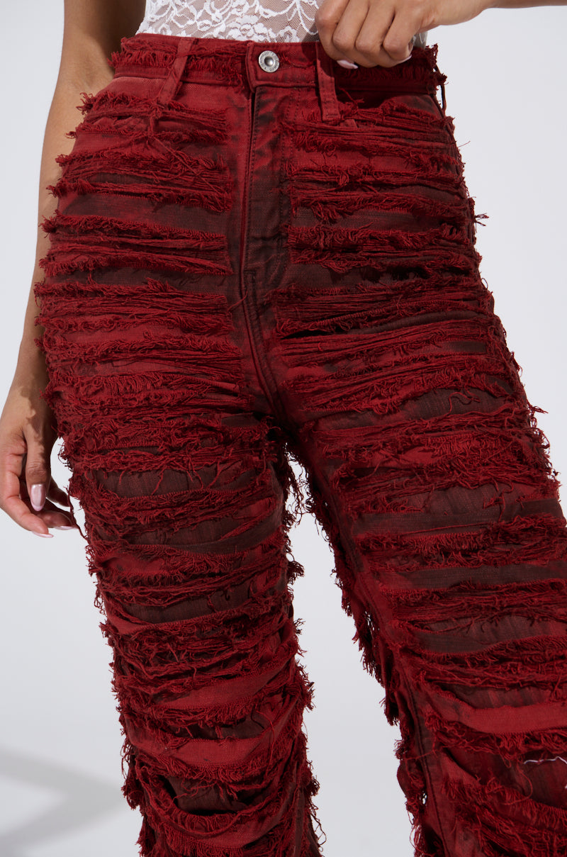 A person sports ON FIRE DISTRESSED DENIM PANT in bright red, featuring distressed layers for texture. The pants have a relaxed fit, a high waist, and silver button closure. Only a hint of white lace from the top is visible against the plain white background.