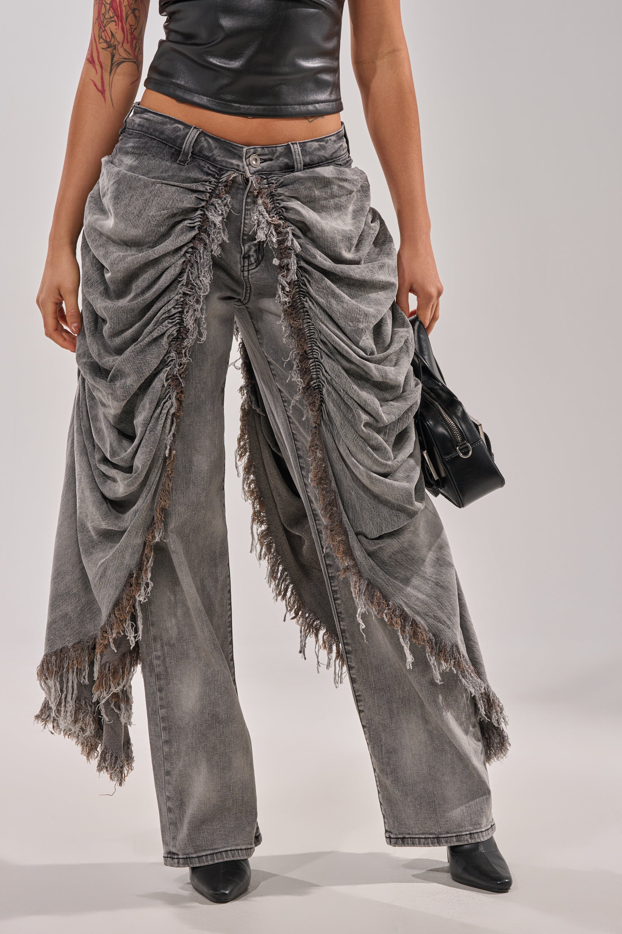 A person wears the WOW WOW WOW DENIM PANT in gray with heavy ruching, styled streetwear fashion, paired with a black sleeveless top, black pointed-toe shoes, and a small black handbag against a neutral background. 2