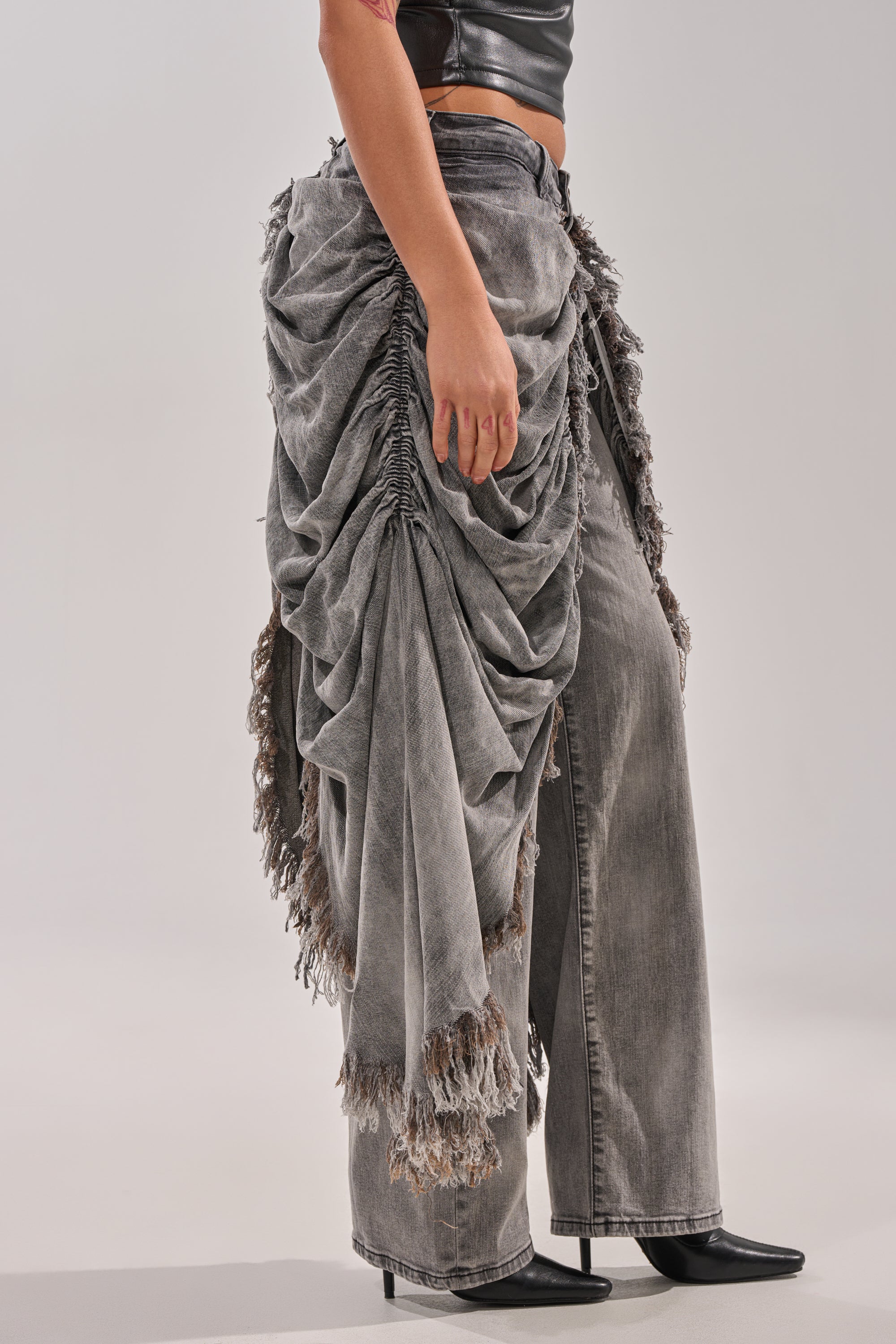 Wearing the WOW WOW WOW DENIM PANT in distressed gray with frayed edges, paired with a black sleeveless top and black pointed-toe heeled boots, a person stands against a plain light background. 3
