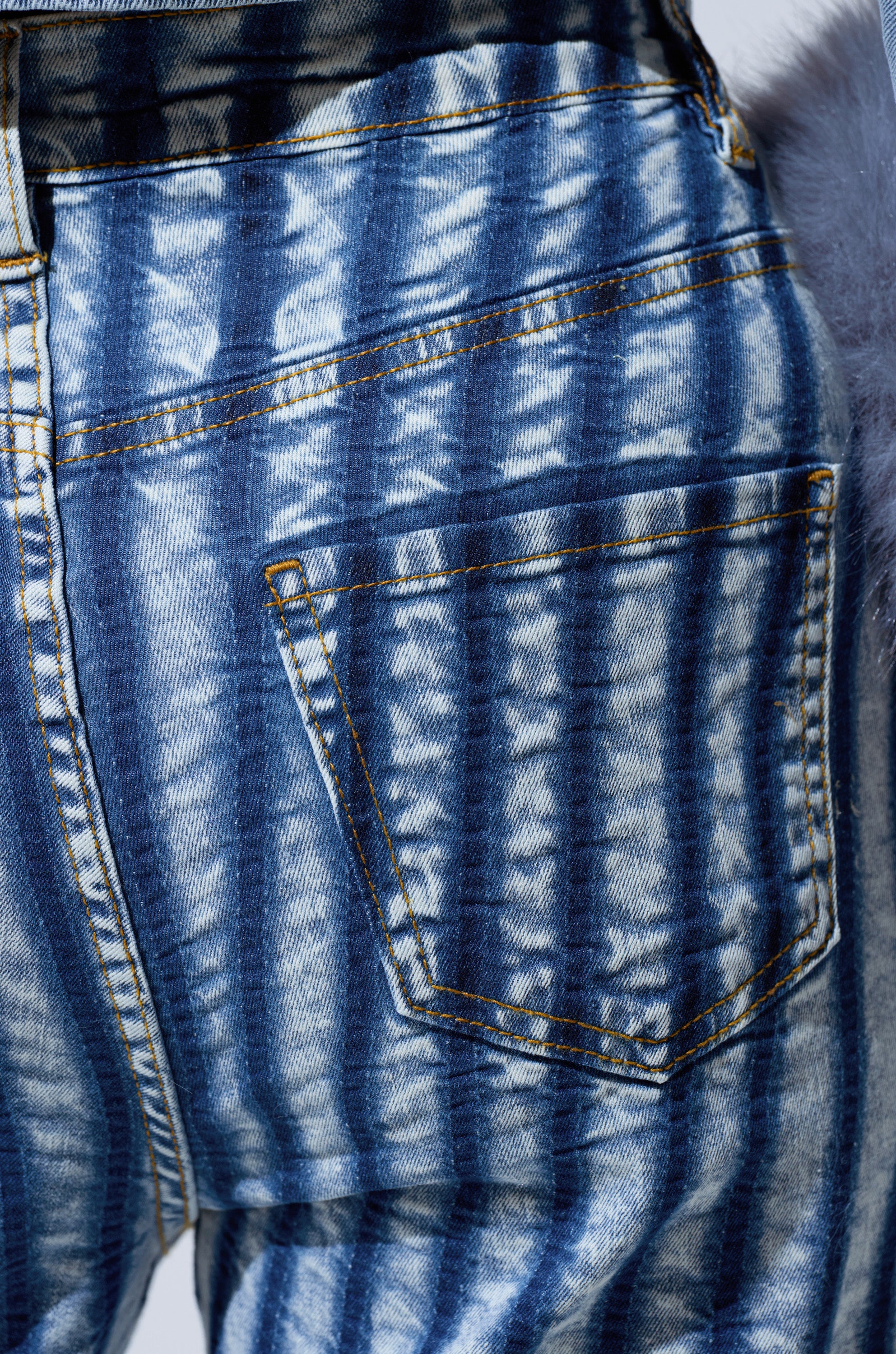 Close-up of the LETS GET CRAZY STRIPE WIDE LEG DENIM's back pocket shows blue stripes, visible yellow stitching, and a striking tie-dye pattern—ideal for fans of high-rise jeans with unique details.
